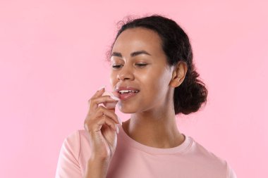 Gülümseyen kadın pembe arka planda dudaklarına merhem sürüyor.