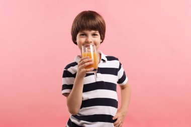 Küçük şirin çocuk pembe arka planda portakal suyu içiyor. Tazeleyici içecek.