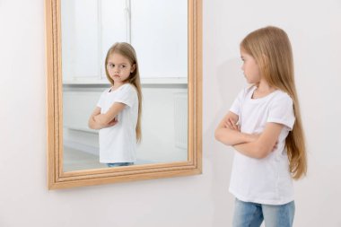 Üzgün küçük kız aynada kendine bakıyor.