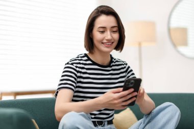 Evdeki koltukta modern akıllı telefon kullanan bir kadın.