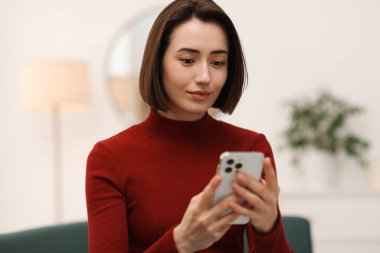 Evdeki koltukta modern akıllı telefon kullanan bir kadın.