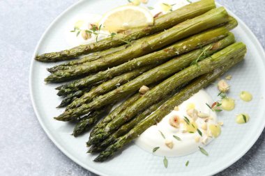 Lezzetli pişmiş kuşkonmaz, limon ve sosla servis edilir. Gri masada, yakın plan.