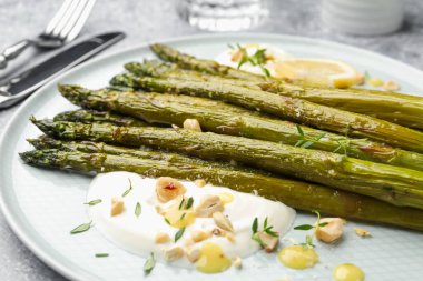 Lezzetli pişmiş kuşkonmaz, limon ve sosla servis edilir. Gri masada, yakın plan.