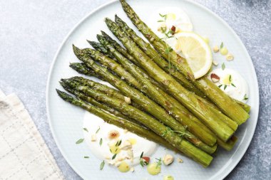 Lezzetli pişmiş kuşkonmaz, limon ve sos ile servis edilir. Gri masa, üst manzara.