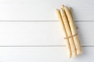 Beyaz ahşap masada bir sürü çiğ kuşkonmaz mızrağı, üst manzara. Metin için boşluk