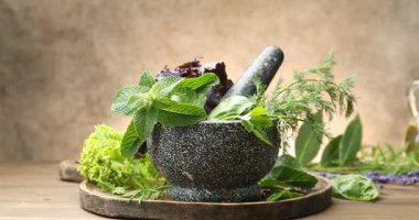 Farklı taze otlarla havan topu ve ahşap masa üzerinde ahşap arka planda, kamera sağa hareket ediyor.