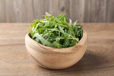 Taze yeşil roka yaprakları ahşap masada kasede, yakın plan.