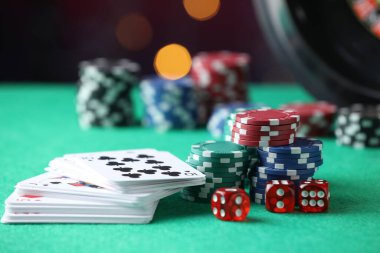 Kumarhane fişleri, zarlar ve iskambil kartları yeşil masada bulanık ışıklara karşı, yakın plan