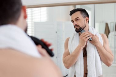 Yakışıklı adam banyoda aynanın yanında tıraş makinesiyle tıraş oluyor.