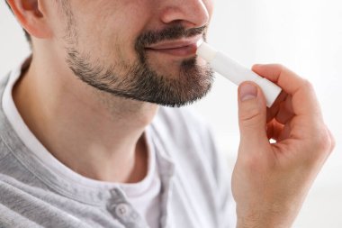 Bulanık ışık arka planında dudaklarına dudak kremi süren bir adam.