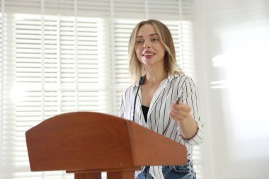 İçerideki kürsüde mikrofonlu bir kadın konuşma yapıyor.