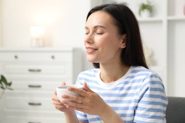 Uyum. Gülümseyen kadın sıcak içecekle evde dinleniyor.