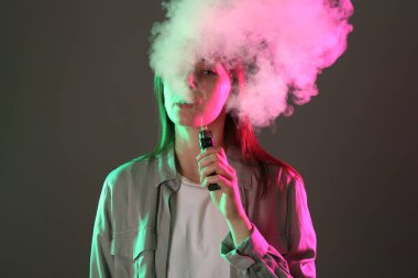 Gri arkaplandaki neon ışıklarda elektronik sigara içen kadın