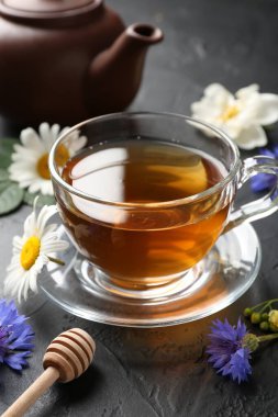 Cam bardakta Aromatik bitki çayı, farklı çiçekler ve siyah masada çaydanlık, yakın plan.