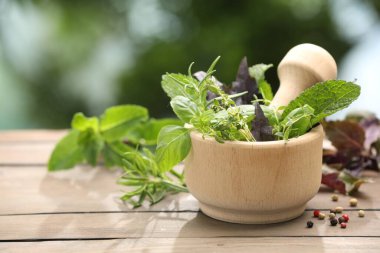 Farklı taze bitkilerle havan topu ve ahşap masa üzerinde bulanık yeşil arka plan, yakın çekim