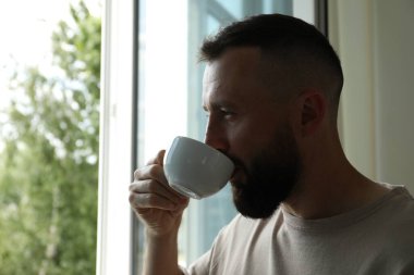 Uyum. Evdeki pencerenin yanında çay içen adam.