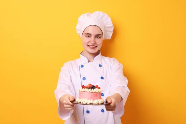 Üniformalı pastacı turuncu arka planda lezzetli bir pasta tutuyor.