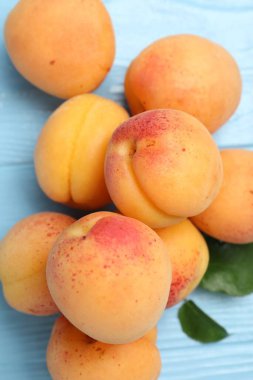 Açık mavi ahşap masada yeşil yapraklı taze kayısılar.