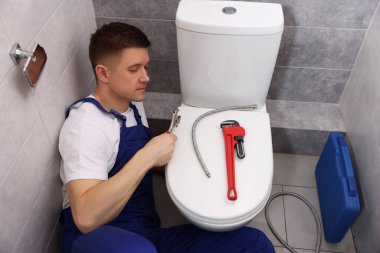 Profesyonel tesisatçı tuvalette klozet tamir ediyor.