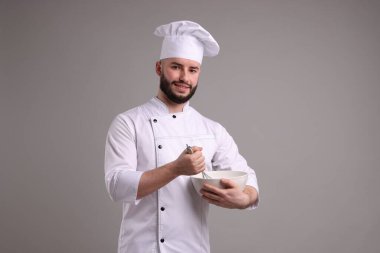 Üniformalı mutlu pastacı açık gri arka planda çırpı ve kase tutuyor.