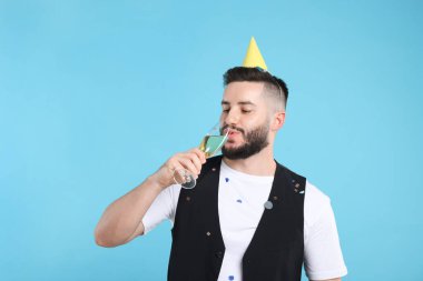 Doğum günün kutlu olsun. Açık mavi arka planda parti şapkası ve bir bardak şampanyası olan yakışıklı bir adam.