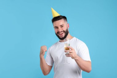 Doğum günün kutlu olsun. Açık mavi arka planda parti şapkası ve bir bardak şampanyası olan yakışıklı bir adam.
