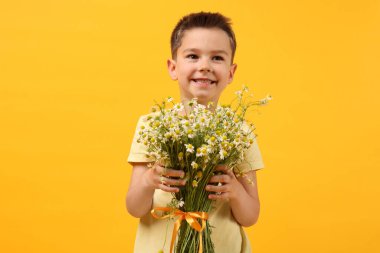 Sarı arka planda bir buket güzel papatya çiçeğiyle gülümseyen küçük çocuk