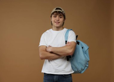 Kahverengi arka planda sırt çantası olan genç bir çocuk.