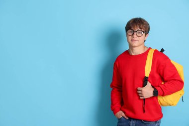 Açık mavi arka planda sırt çantalı, gözlüklü yakışıklı bir genç. Metin için boşluk