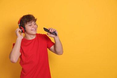 Sarı arka planda akıllı telefonu olan, kulaklıklı, gülümseyen genç bir çocuk. Metin için boşluk
