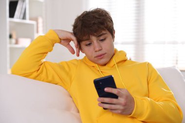 Genç çocuk evdeki kanepede akıllı telefon kullanıyor.