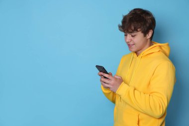 Açık mavi arka planda akıllı telefon kullanan gülümseyen genç çocuk. Metin için boşluk
