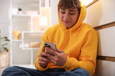 Ergen çocuk evde çekmecelerin yanında akıllı telefon kullanıyor.