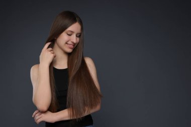 Sağlıklı, uzun saçlı, koyu gri arka planda gülümseyen genç kız. Metin için boşluk