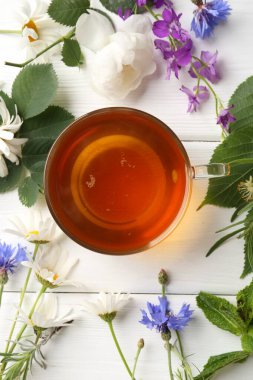 Cam bardakta Aromatik bitki çayı, farklı çiçekler ve beyaz ahşap masada nane şekeri, düz uzanmış.