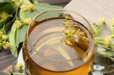 Fincanda taze ıhlamur çayı ve koyu ahşap masada çiçekler, yakın plan.