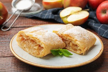 Lezzetli elmalı turta parçaları pudra şekeri, nane ve ahşap masada meyveler, yakın plan.