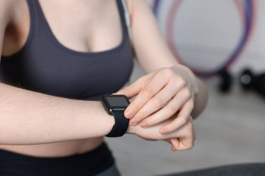 Kadın spor salonunda spor yaparken takip cihazını kontrol ediyor, yakın plan.
