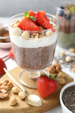 Chia tohumlu çikolatalı puding, çilek, yoğurt ve fındıklar beyaz masada, yakın plan.