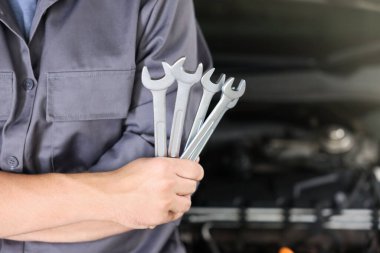 Otomobil parçaları. Kaputu açık, kapalı kaputun yanında anahtarı olan profesyonel bir tamirci, yakın plan. Metin için boşluk