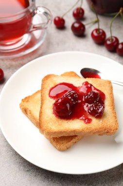 Lezzetli kiraz reçelli tostlar, çay ve taze meyveler gri masada, yakın plan.