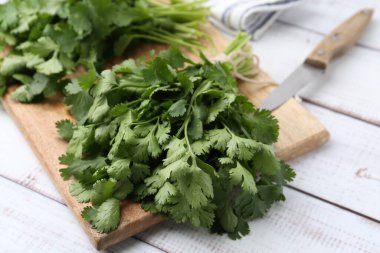 Tahta kesme tahtası taze kişniş ve bıçak beyaz ahşap masada, yakın plan.