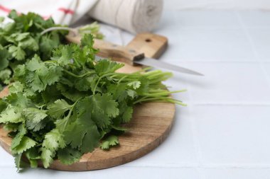 Beyaz fayanslı masada taze kişniş ve bıçakla kesme tahtası, yakın plan. Metin için boşluk
