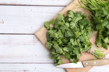 Beyaz ahşap masada taze kişniş ve bıçakla kesme tahtası, üst manzara. Metin için boşluk