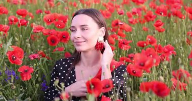 Gülen kadın kır çiçeklerinde kırmızı gelincik çiçekleri arasında poz veriyor.