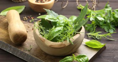 Bir kadın ahşap masada farklı taze otlara sıkar ve dokunur.