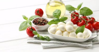 Lezzetli mozzarella peyniri, domates, fesleğen ve baharatlar beyaz ahşap masada, yakın plan. Kamera hareket ediyor