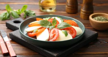 Peynirli Caprese salatası, domates ve fesleğenli ahşap masa, yakın plan. Kamera içeri giriyor.