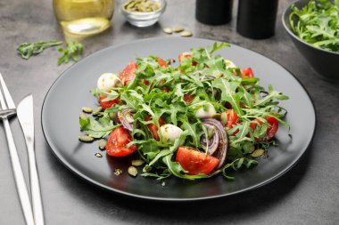 Lezzetli salata roka, mozzarella ve sebzeler gri masada servis edilir, yakın plan.