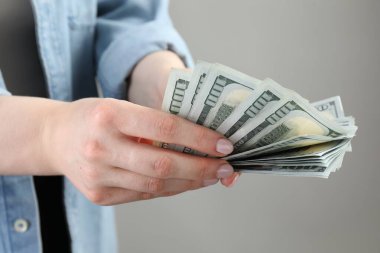 Açık gri arka planda dolar banknotları sayan kadın, yakın plan